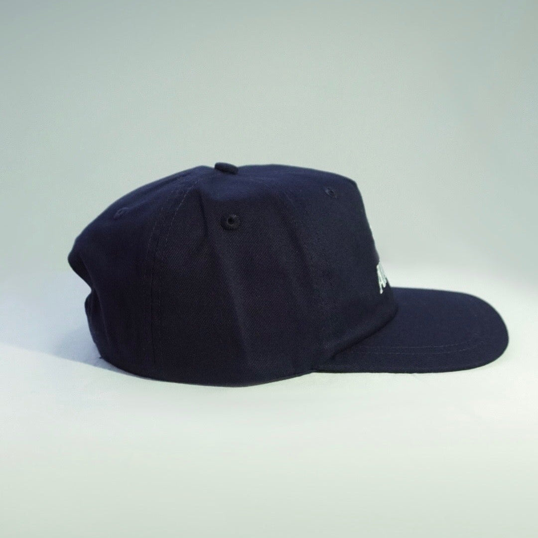 A dark navy blue baseball cap with a curved brim, photographed from the side against a light gray studio background.