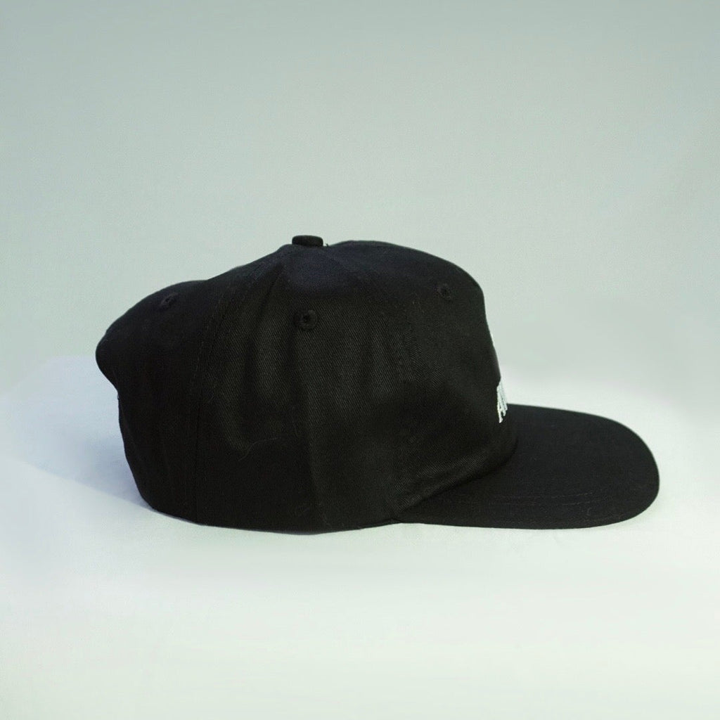 A black baseball cap with a curved brim, photographed from the side against a light gray studio background.