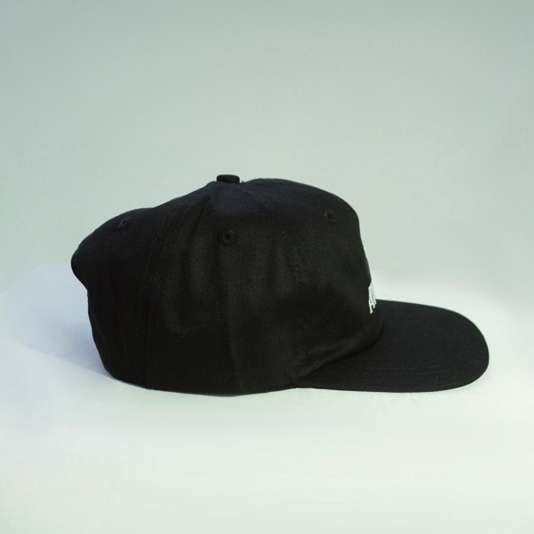 A black baseball cap with a curved brim, photographed from the side against a light gray studio background.