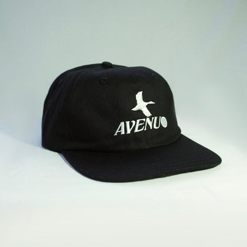 A black flat-brim baseball cap with a white embroidered bird logo and the word 'AVENUE' on the front, photographed against a light gray studio background.