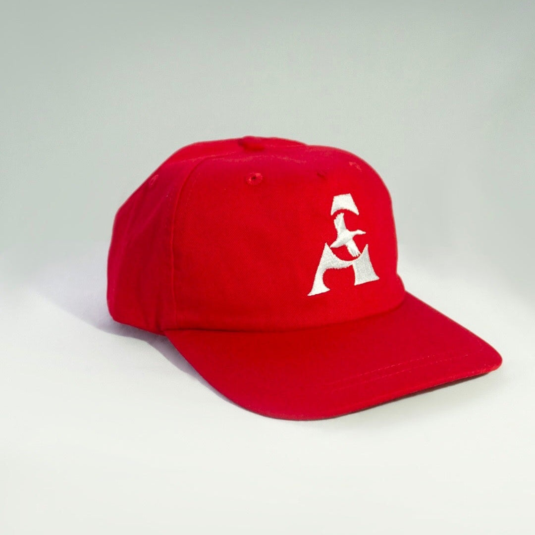 A red baseball cap with a white embroidered geometric logo on the front, photographed on a light gray studio background.
