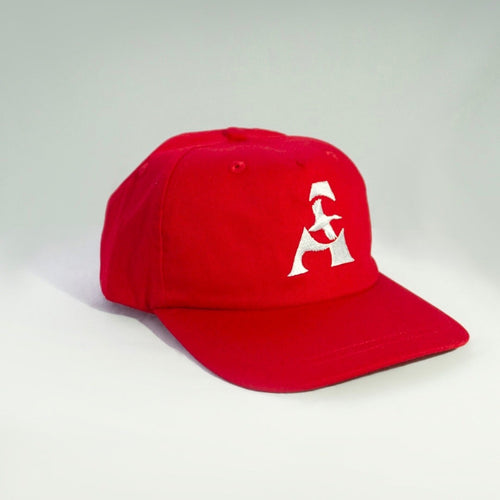 A red baseball cap with a white embroidered geometric logo on the front, photographed on a light gray studio background.