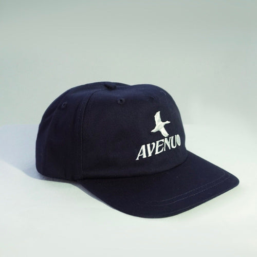 A dark navy blue baseball cap with a curved brim, featuring a white embroidered bird logo and the word 'AVENUE' on the front, set against a light gray studio background.